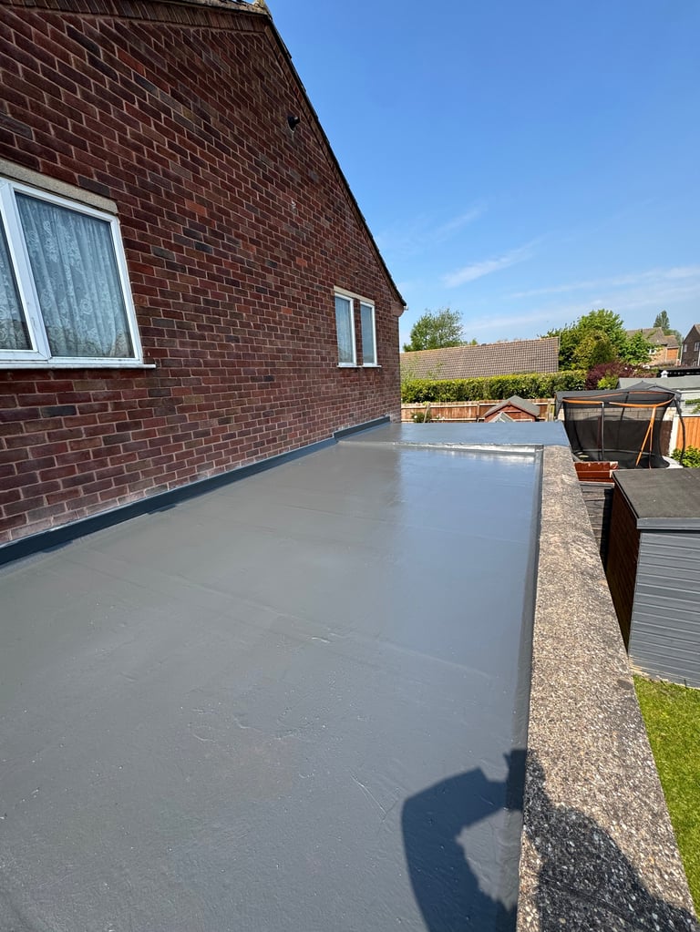Flat roof with gray waterproof membrane on brick house with clear blue sky and garden in background
