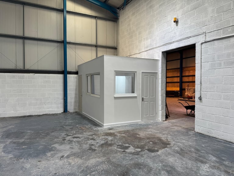 White modular office building inside a warehouse with concrete floor and industrial overhead door visible