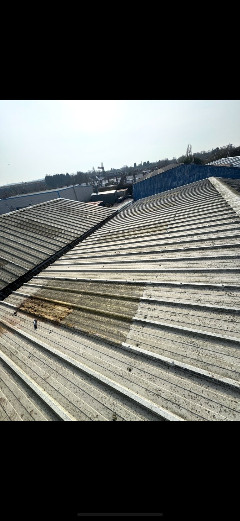 Industrial metal rooftop with corrugated panels overlooking urban cityscape with church spire and forested skyline