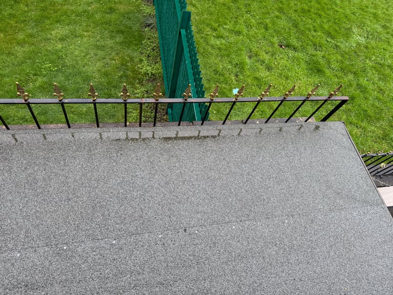 Aerial view of a metal fence dividing a concrete patio from a lush green lawn with a green umbrella