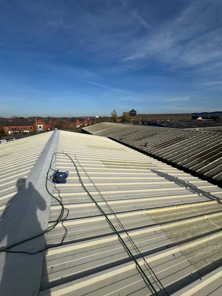 Industrial corrugated metal rooftop with electrical cables and equipment, overlooking suburban landscape