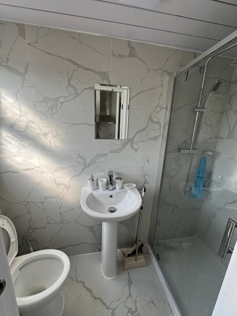 Modern bathroom interior with marble-patterned tiles, white pedestal sink, toilet, mirrored cabinet, and glass shower enclosure