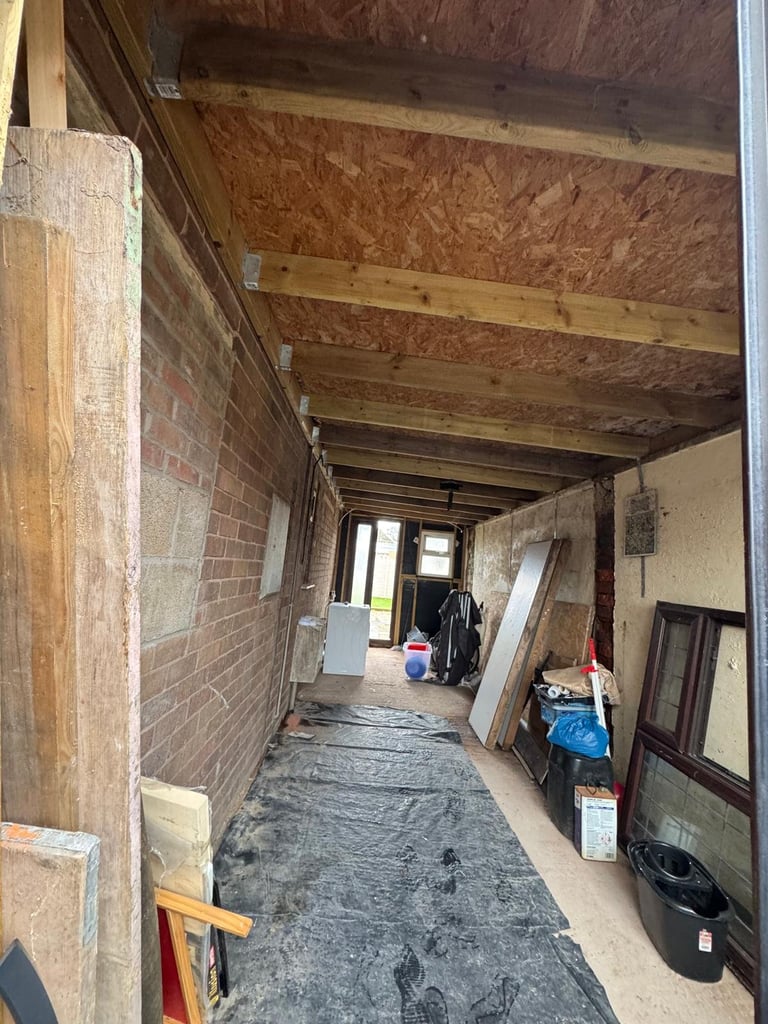 Interior of a renovation project showing brick walls, wooden beam ceiling, and construction materials along the hallway.